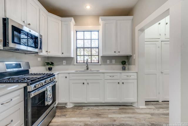 kitchen with light wood-type flooring, appliances with stainless steel finishes, sink, and white cabinets