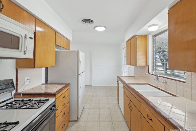 kitchen with tile countertops, decorative backsplash, white appliances, and sink