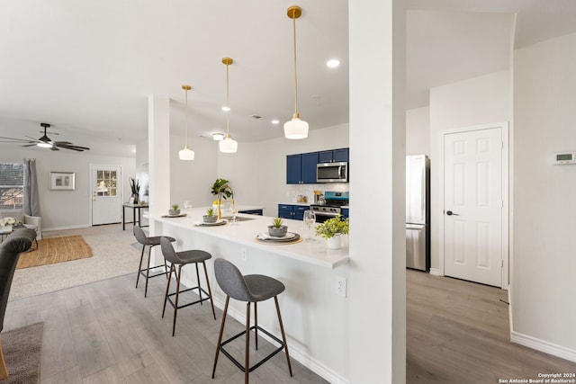 kitchen featuring kitchen peninsula, appliances with stainless steel finishes, a kitchen bar, blue cabinets, and ceiling fan