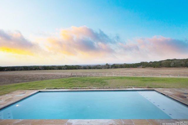 pool at dusk featuring a rural view and a lawn