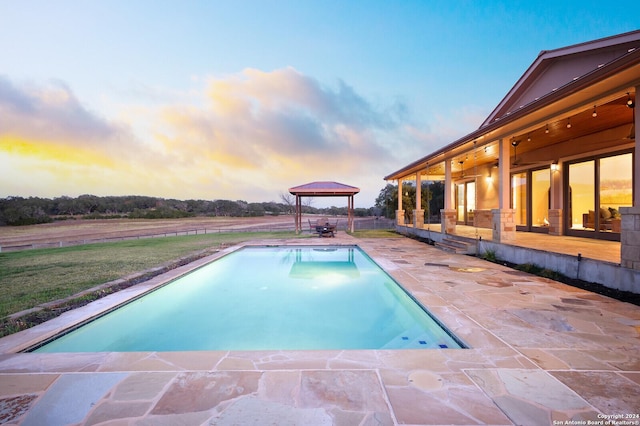 pool at dusk featuring a gazebo and a patio area