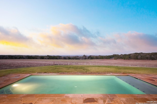 pool at dusk featuring a lawn and a rural view