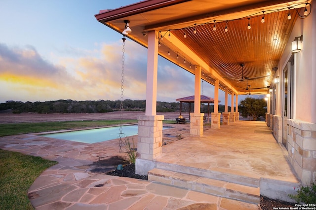 pool at dusk with ceiling fan and a patio