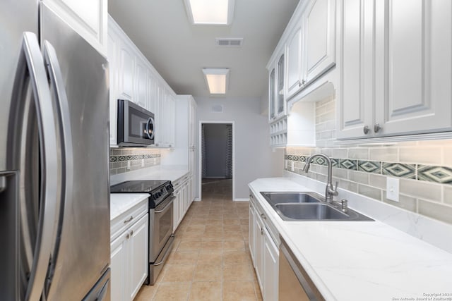 kitchen featuring light stone countertops, backsplash, stainless steel appliances, sink, and white cabinetry