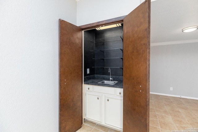 interior space with white cabinets, light tile patterned floors, ornamental molding, and sink