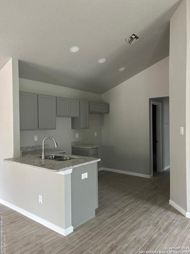 kitchen featuring gray cabinetry, sink, vaulted ceiling, light wood-type flooring, and kitchen peninsula