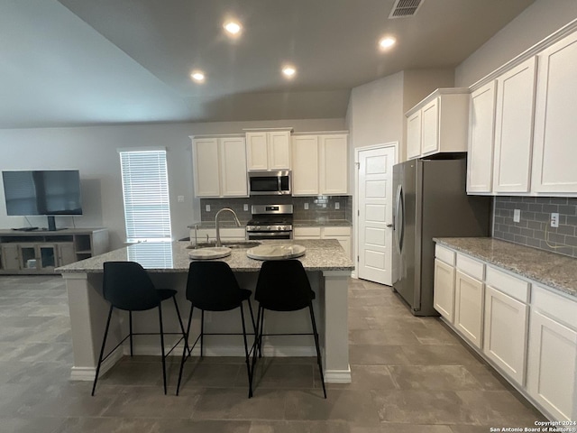 kitchen featuring light stone countertops, a center island with sink, white cabinets, and appliances with stainless steel finishes