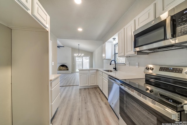 kitchen featuring light wood-type flooring, stainless steel appliances, vaulted ceiling, sink, and white cabinets