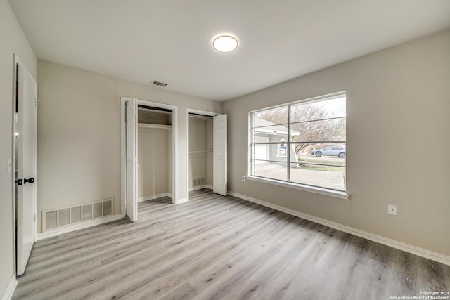 unfurnished bedroom featuring multiple closets and light wood-type flooring