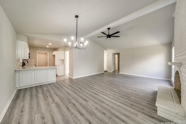 unfurnished living room featuring lofted ceiling with beams, ceiling fan with notable chandelier, sink, a brick fireplace, and light hardwood / wood-style floors