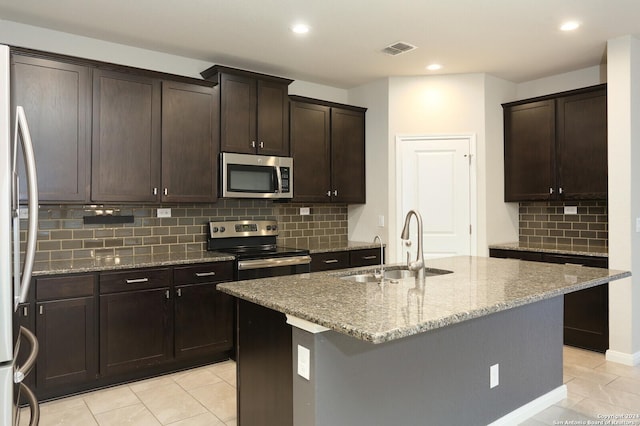 kitchen with a center island with sink, sink, appliances with stainless steel finishes, tasteful backsplash, and light stone counters