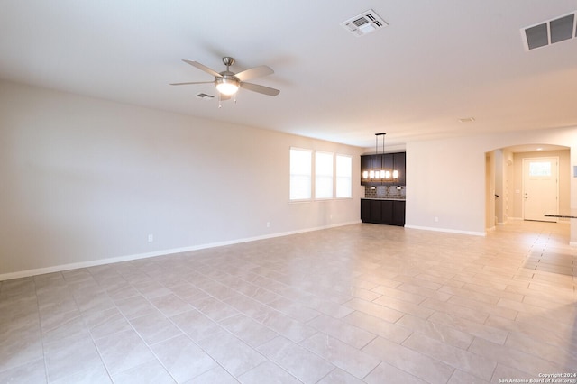 tiled empty room featuring ceiling fan with notable chandelier