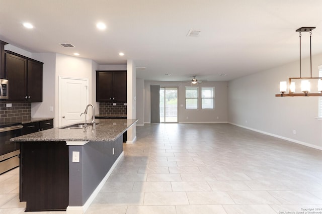 kitchen with light stone counters, dark brown cabinetry, ceiling fan, a kitchen island with sink, and sink