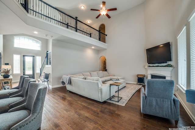 living room with ceiling fan, a towering ceiling, and dark wood-type flooring