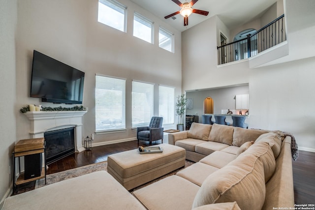 living room with ceiling fan, dark hardwood / wood-style flooring, a towering ceiling, and a healthy amount of sunlight