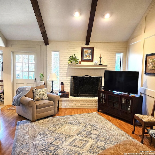 living room with hardwood / wood-style flooring, vaulted ceiling with beams, brick wall, and a brick fireplace