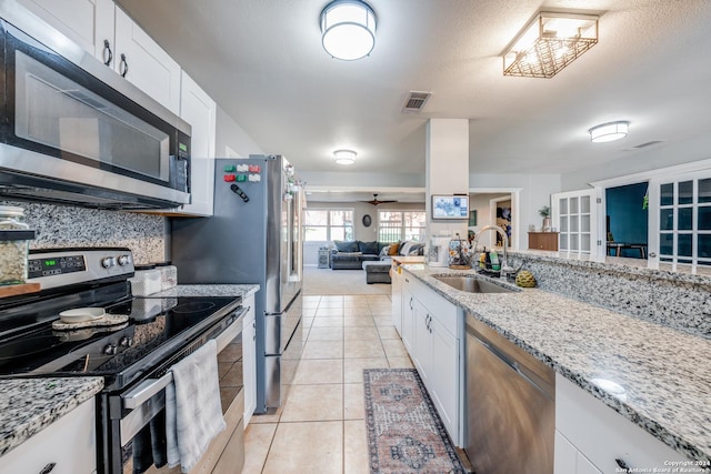 kitchen with appliances with stainless steel finishes, light stone counters, ceiling fan, sink, and white cabinets