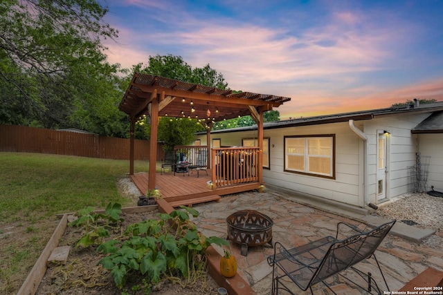 deck at dusk featuring a pergola, a yard, and a fire pit