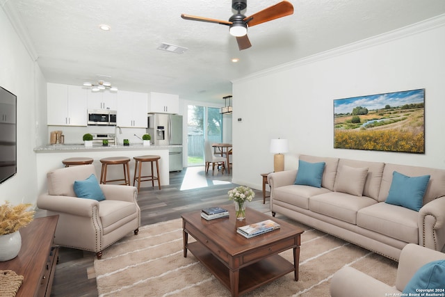 living room with a textured ceiling, ceiling fan, crown molding, sink, and light hardwood / wood-style floors