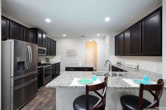 kitchen featuring sink, dark wood-type flooring, stainless steel appliances, decorative backsplash, and a breakfast bar