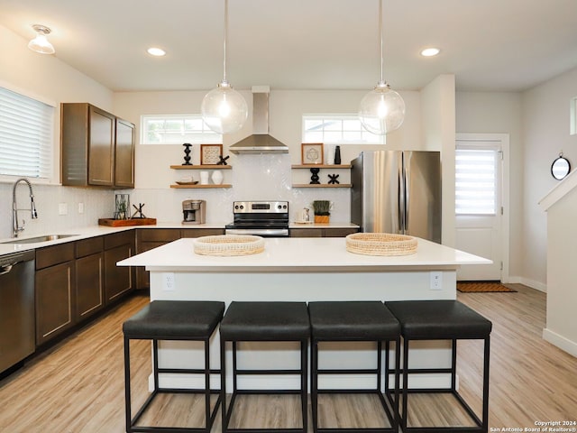 kitchen featuring wall chimney exhaust hood, a center island, sink, and appliances with stainless steel finishes