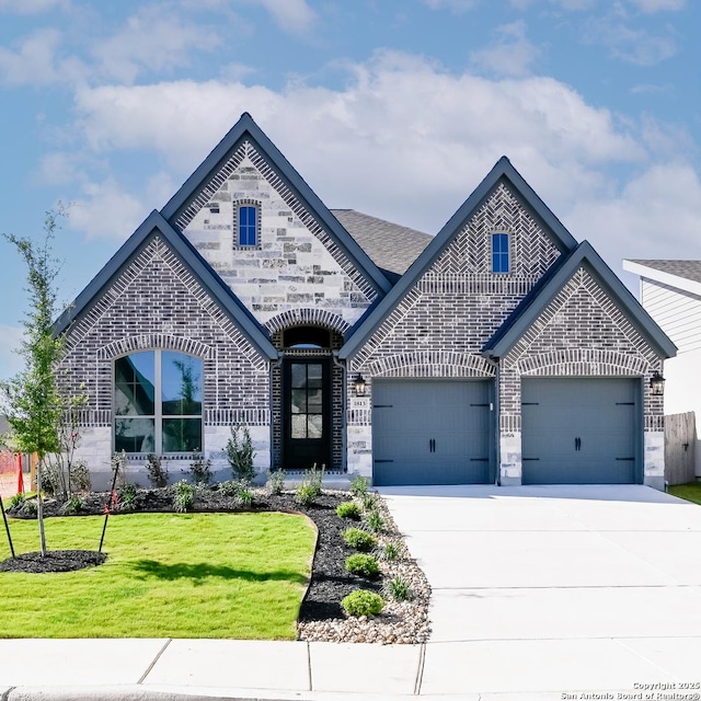 french country style house featuring an attached garage, a front lawn, stone siding, brick siding, and driveway
