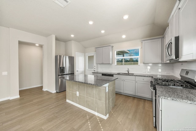 kitchen with appliances with stainless steel finishes, vaulted ceiling, sink, light hardwood / wood-style flooring, and a kitchen island