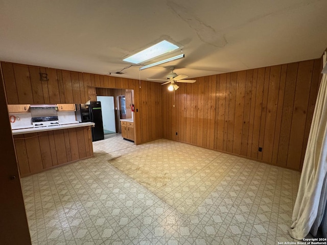 kitchen with a skylight, ceiling fan, black fridge, white range, and wood walls