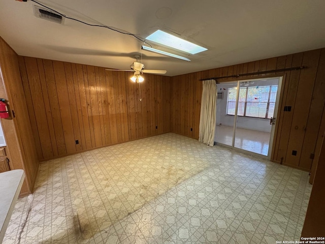 empty room featuring a skylight, ceiling fan, and wooden walls