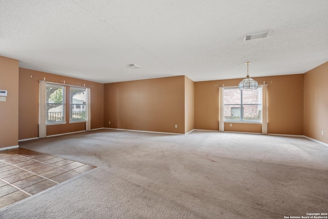 carpeted empty room with a notable chandelier, plenty of natural light, and a textured ceiling