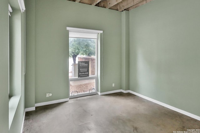 empty room featuring beam ceiling and concrete flooring