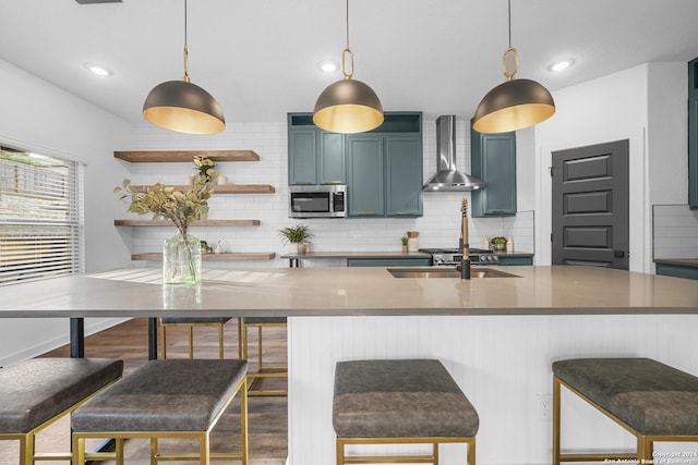 kitchen with blue cabinetry, a kitchen breakfast bar, wall chimney range hood, and hanging light fixtures