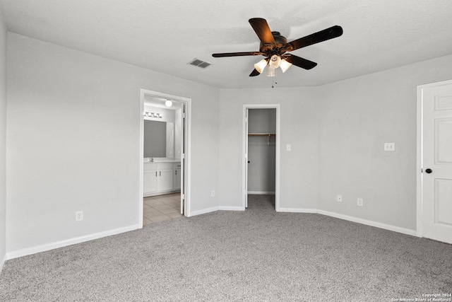 unfurnished bedroom featuring ceiling fan, light colored carpet, a walk in closet, and a textured ceiling