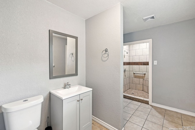 bathroom with tile patterned flooring, toilet, a tile shower, and a textured ceiling