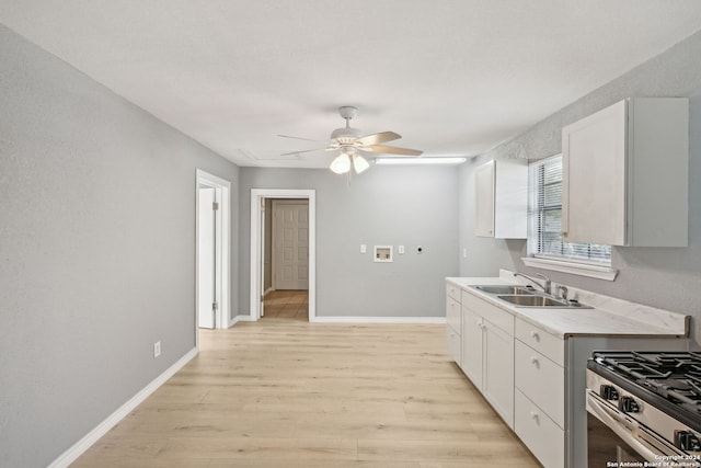 kitchen with light wood-type flooring, stainless steel gas range oven, ceiling fan, sink, and white cabinets