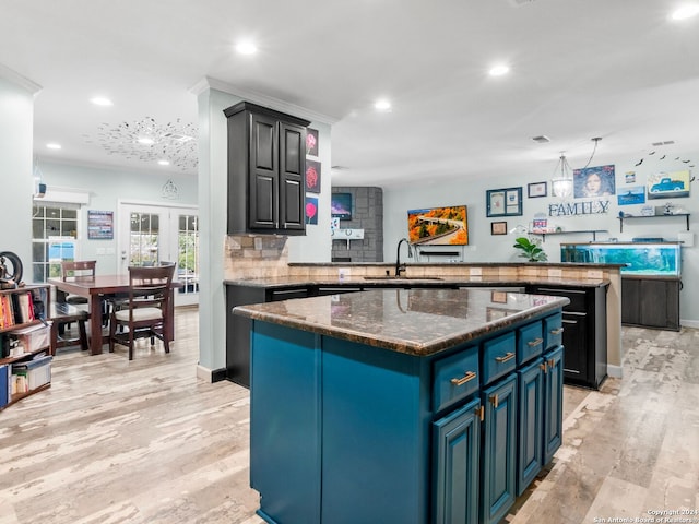 kitchen featuring blue cabinets, kitchen peninsula, dark stone countertops, light hardwood / wood-style floors, and a kitchen island