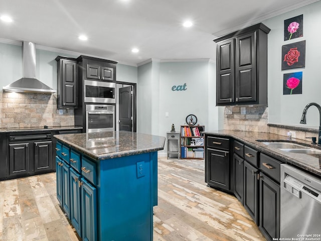 kitchen with wall chimney range hood, sink, dark stone countertops, appliances with stainless steel finishes, and a kitchen island