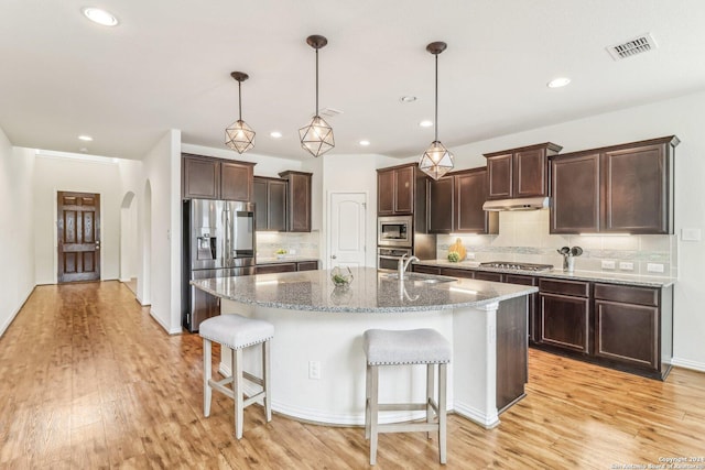 kitchen with tasteful backsplash, a kitchen island with sink, stainless steel appliances, and light wood-type flooring