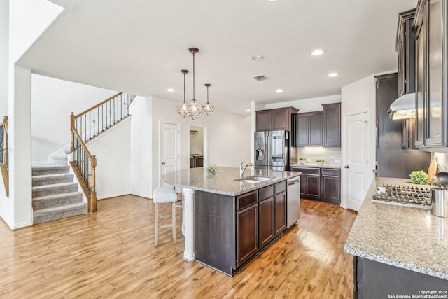 kitchen with sink, hanging light fixtures, light hardwood / wood-style floors, a kitchen island with sink, and appliances with stainless steel finishes