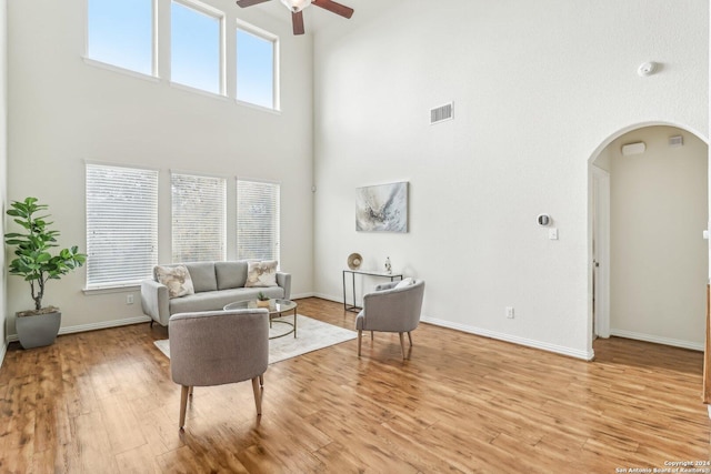 living room with ceiling fan, a towering ceiling, and light wood-type flooring