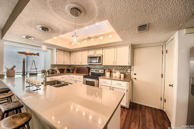 kitchen with sink, appliances with stainless steel finishes, a tray ceiling, decorative light fixtures, and a breakfast bar area