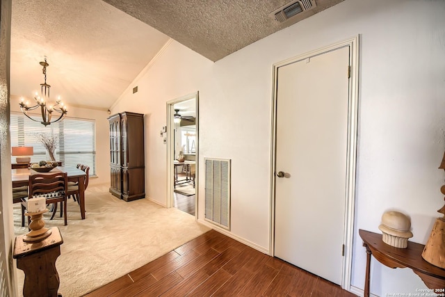 corridor featuring a textured ceiling, hardwood / wood-style floors, vaulted ceiling, and a notable chandelier