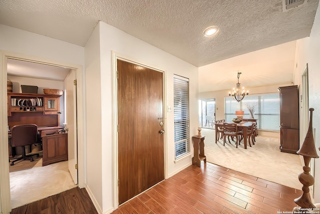 foyer entrance with wood-type flooring, a textured ceiling, and a chandelier