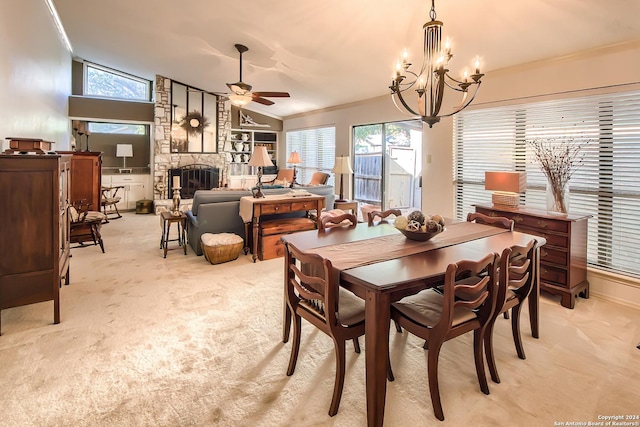 dining room featuring lofted ceiling, ceiling fan with notable chandelier, a stone fireplace, crown molding, and light colored carpet