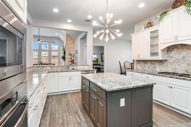 kitchen featuring white cabinetry, stainless steel appliances, a kitchen island, ceiling fan with notable chandelier, and hardwood / wood-style flooring