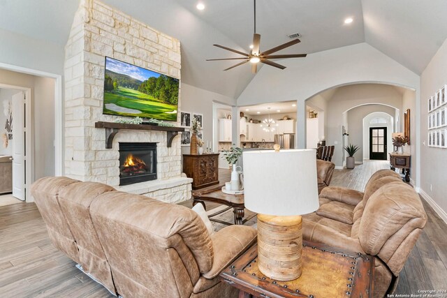 living room with light hardwood / wood-style floors, a stone fireplace, ceiling fan, and lofted ceiling