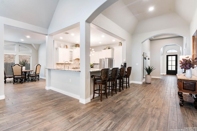 kitchen with kitchen peninsula, light stone counters, vaulted ceiling, white cabinets, and stainless steel refrigerator