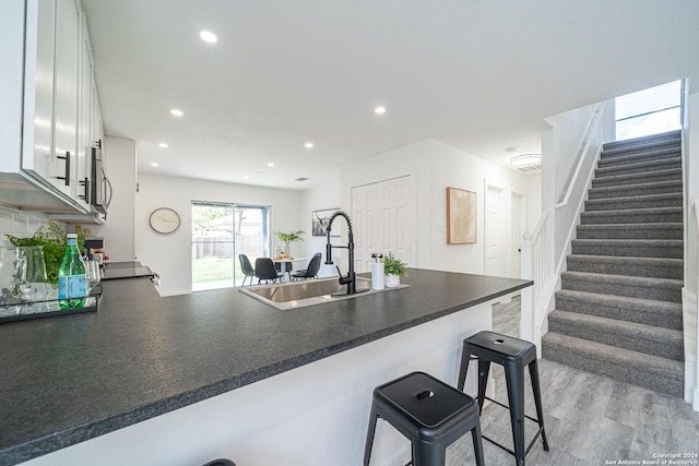 kitchen with kitchen peninsula, white cabinetry, a breakfast bar area, and sink