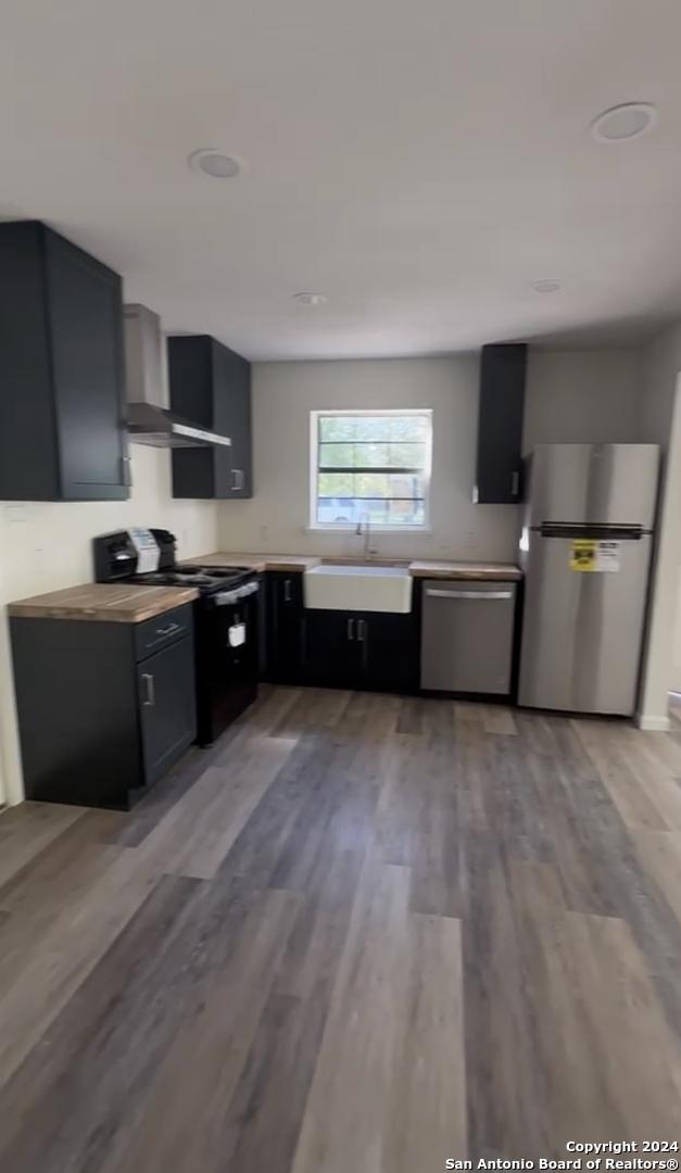 kitchen with wall chimney range hood, appliances with stainless steel finishes, light wood-type flooring, and sink