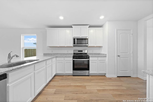 kitchen with white cabinetry, sink, stainless steel appliances, light stone counters, and light hardwood / wood-style flooring